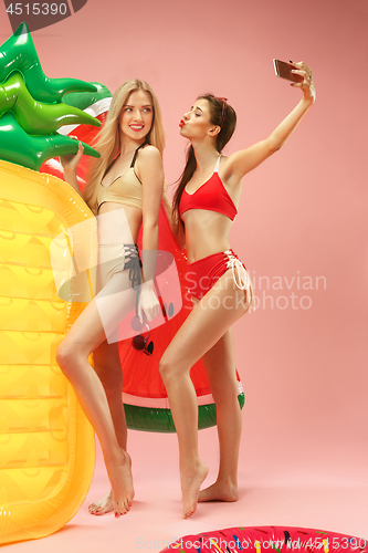 Image of Cute girls in swimsuits posing at studio. Summer portrait caucasian teenagers on pink background.