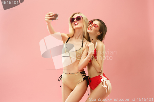 Image of Cute girls in swimsuits posing at studio. Summer portrait caucasian teenagers on pink background.