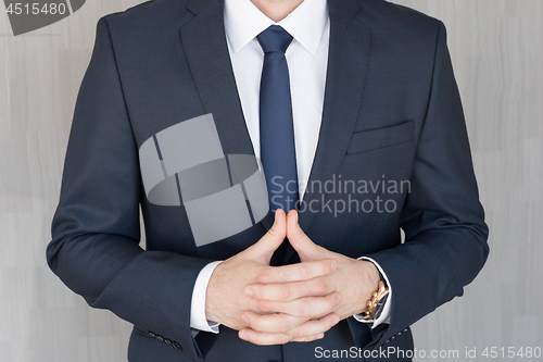 Image of Torso of anonymous businessman standing with hands in lowered steeple, wearing beautiful fashionable classic navy blue suit.