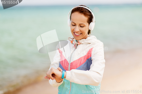 Image of woman with fitness tracker and headphones on beach