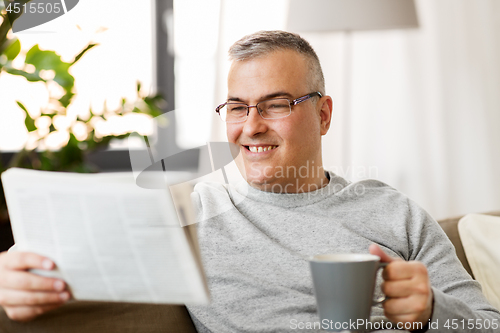 Image of man reading newspaper and drinking coffee at home