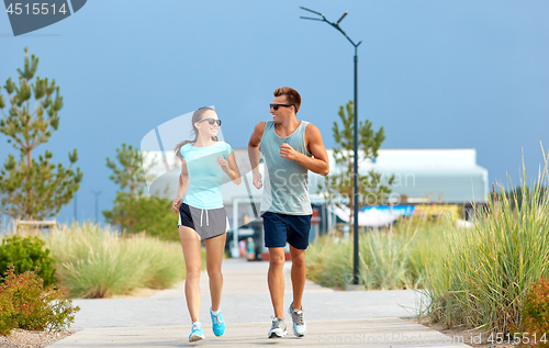 Image of couple in sports clothes running along on beach