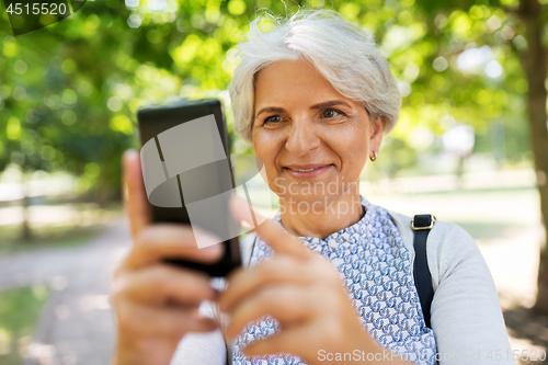 Image of senior woman photographing by cell at summer park