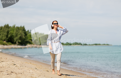 Image of woman with headphones walking along summer beach