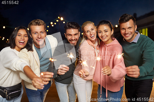 Image of happy friends with sparklers at rooftop party