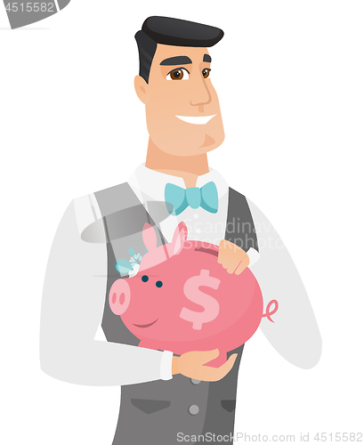 Image of Caucasian groom holding a piggy bank.