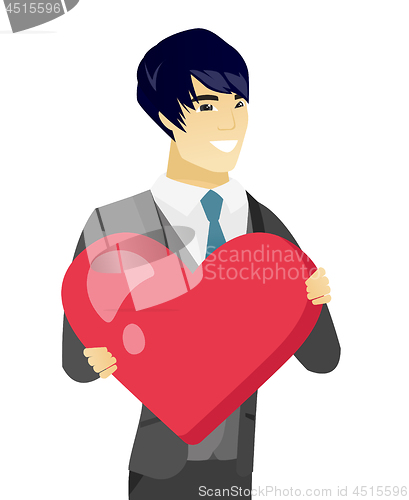 Image of Young asian groom holding a big red heart.