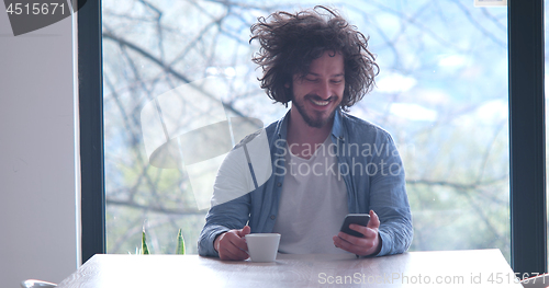 Image of young man drinking coffee and using a mobile phone  at home