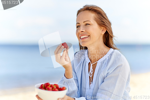 Image of happy woman eating strawberries on summer beach