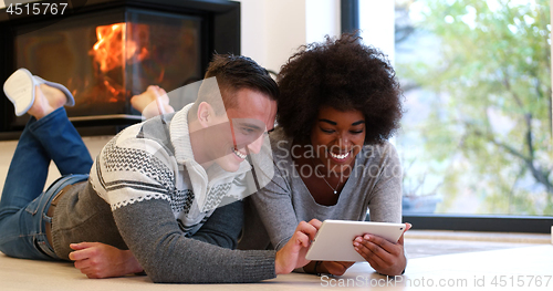 Image of multiethnic couple using tablet computer on the floor