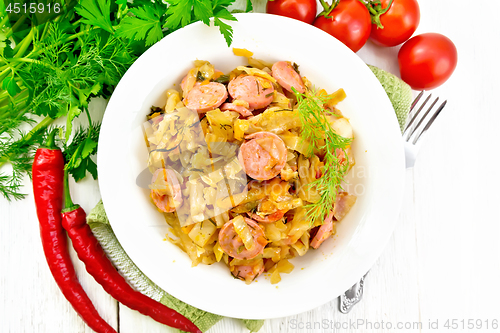 Image of Cabbage stew with sausages in white plate on light board top