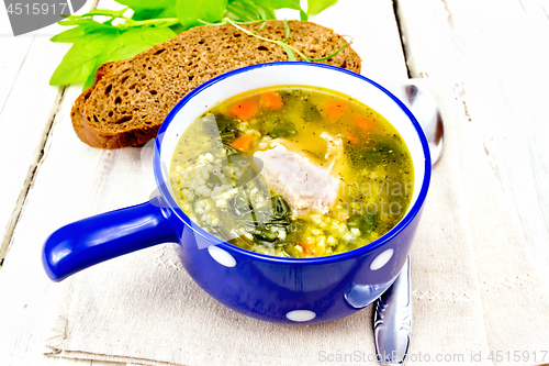Image of Soup with couscous and spinach in blue bowl on light board