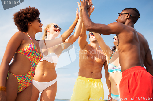 Image of happy friends making high five on summer beach