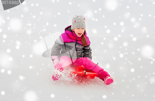 Image of happy little girl sliding down on sled in winter