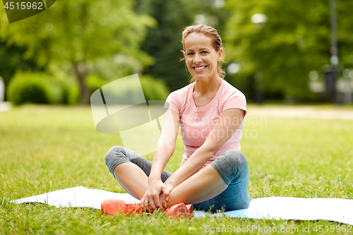 Image of woman sitting on exercise mat at park in summer