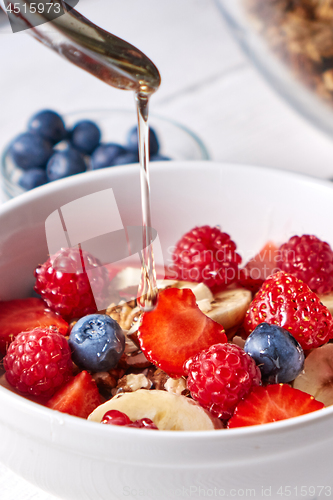 Image of Healthy breakfast with fresh honey is pured into the flakes, muesli, raspberries, blueberries, strawberries on a gray wooden table. Close-up.