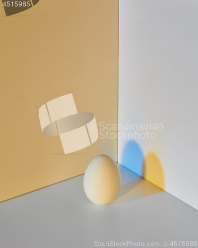 Image of Painted egg on a gray-yellow double background with a reflection of blue-yellow shadows and copy space for text. Easter layout