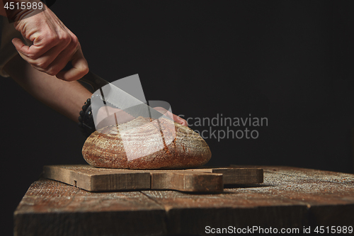 Image of man slicing fresh organic bread on wooden board