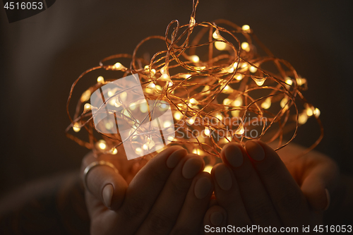 Image of Woman hands holding string of lights in the dark.