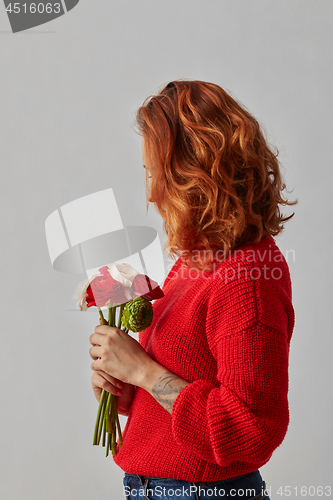 Image of Young woman with lush red hair with a bunch of fresh Ranunculus on gray background with copy space.