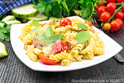 Image of Fusilli with chicken and tomatoes in plate on black wooden board