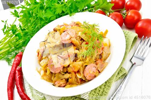 Image of Cabbage stew with sausages in white plate on light board