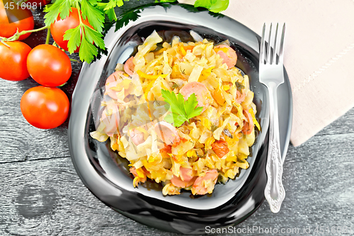 Image of Cabbage stew with sausages in black plate on board top