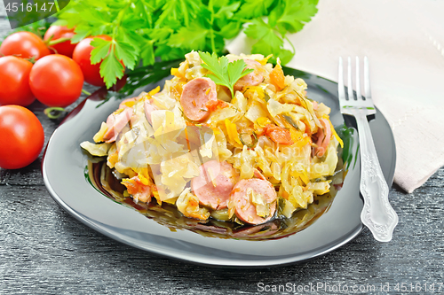 Image of Cabbage stew with sausages in black plate on wooden board