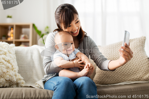 Image of happy mother with baby son taking selfie at home