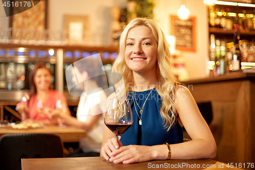 Image of happy woman drinking red wine at bar or restaurant