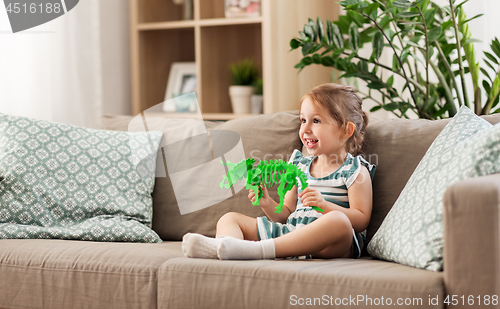 Image of happy baby girl playing with toy dinosaur at home