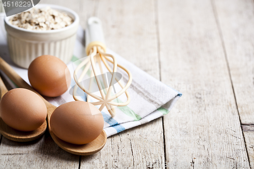 Image of Fresh chicken eggs, oat flakes in ceramic bowl and kitchen utens