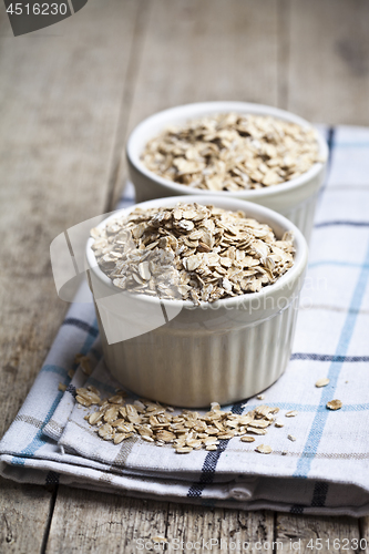 Image of Raw oat flakes in ceramic bowls on linen napkin, golden wheat ea