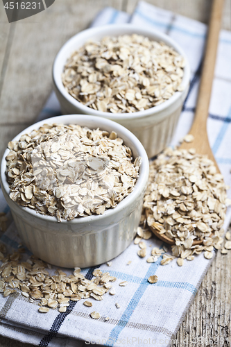 Image of Oat flakes in ceramic bowls and wooden spoon on linen napkin, go