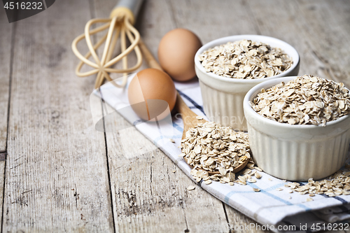 Image of Fresh chicken eggs, oat flakes in ceramic bowls and wooden spoon