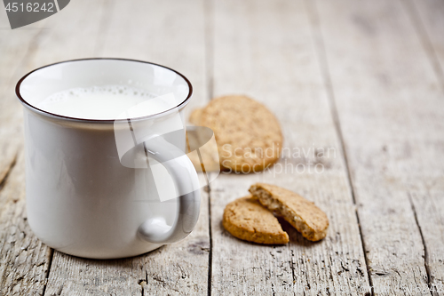 Image of Cup of milk and some fresh baked oat cookies on rustic wooden ta