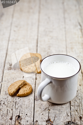 Image of Cup of milk and some fresh baked oat cookies on rustic wooden ta