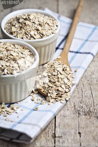 Image of Oat flakes in ceramic bowls and wooden spoon on linen napkin, go