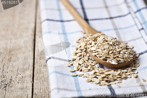 Image of Oat flakes in wooden spoon on linen napkin, golden wheat ears on