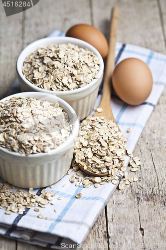 Image of Oat flakes in ceramic bowls and wooden spoon and fresh chicken e