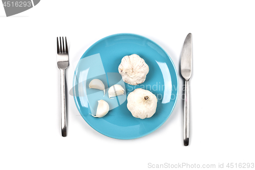 Image of Organic garlic on blue plate, fork and knife on white background