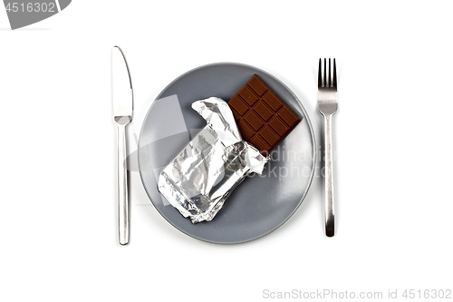 Image of Chocolate bar with foil on blue plate, fork and knife on white b