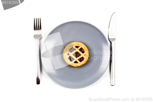 Image of Chocolate tart on grey ceramic plate, fork and knife on white ba