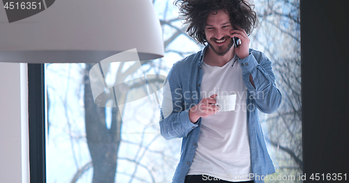 Image of young man drinking coffee and using a mobile phone  at home