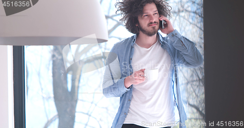 Image of young man drinking coffee and using a mobile phone  at home