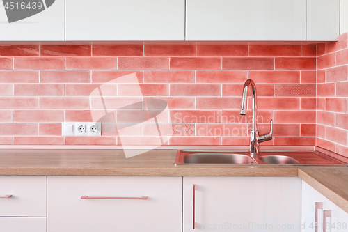 Image of Interior corner of the modern kitchen with steel sink and wall tiles in a trend color of the year 2019 Living Coral Pantone.