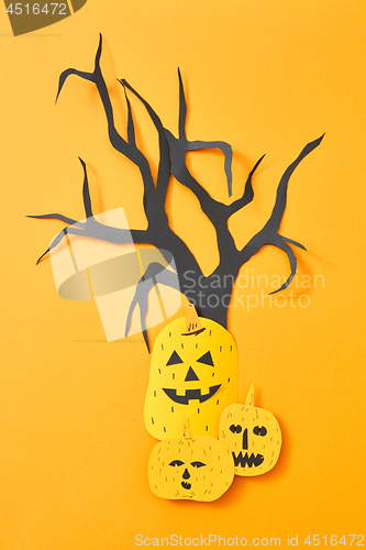 Image of Handcraft paper tree and scary pumpkins on an orange background with space for text. Halloween layout. Flat lay