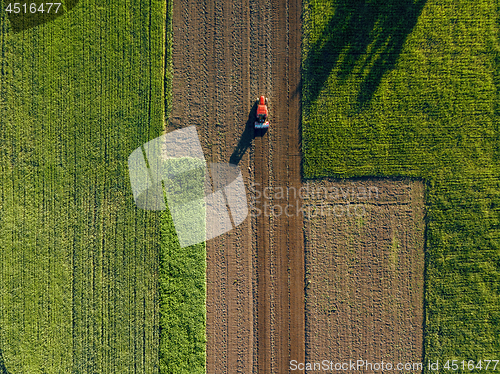 Image of Aerial view from the drone, a bird\'s eye view of agricultural fields with a road through and a tractor on it in the spring evening at sunset in the summer