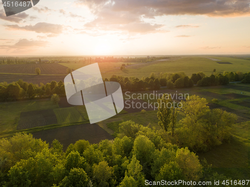 Image of Aerial view from the drone, a bird\'s eye view of abstract geometric forms of agricultural fields with a dirt road through them in the summer evening at sunset.