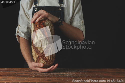 Image of Baker\'s hands hold an oval bread.